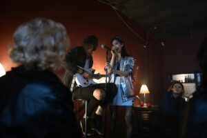 Asian woman sings with guitarist at a cozy bar during a lively night performance.